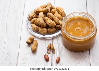 Jar of peanut butter, bunch of peanuts on white wooden table. Homemade peanut butter, natural, organic product. Modern wellness and vegan concept, raw food diet.