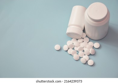 A Jar And Scattered White Pills On A Blue Background. Medicine, Health, Vitamins, Drug Manufacturing. Free Space For Text.