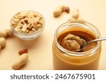 Jar and spoon of peanut butter on beige background. Top view