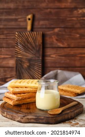 Jar With Sweet Condensed Milk And Waffles On Wooden Background