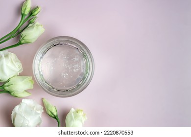 Jar With Transparent Cosmetic Product, Gel Or Cream On Rose Colored Background With Flowers. Unbranded Package With Antioxidant Cream For Self-care. View From Above.