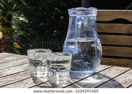 The jar and two glasses of cold clear water on the wooden table, shining in the sun