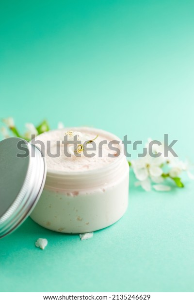 Jar of white skincare cream with Fresh spring\
cherry blossom flowers. Cosmetic bottles. Botanical spa treatment\
delicate skin. turquoise\
background