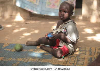 Jarra, Gambia, Africa, May 2, 2019: Horizontal Closeup Photography Of A Small Boy In Too Big Gray Tshirt, Holding A New Car, Sitting Outdoors On A Sunny Day