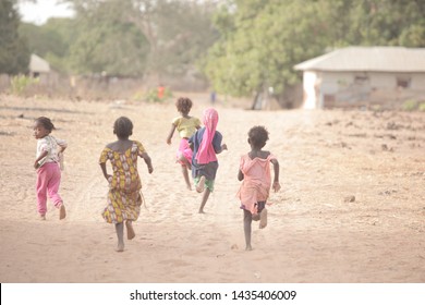 Jarra, The Gambia, Africa, May 28, 2018: Horizontal Photography Of A Group Of Barefoot Kids Running Away From The Camera On A Dirt Road, Outdoors On A Sunny Day