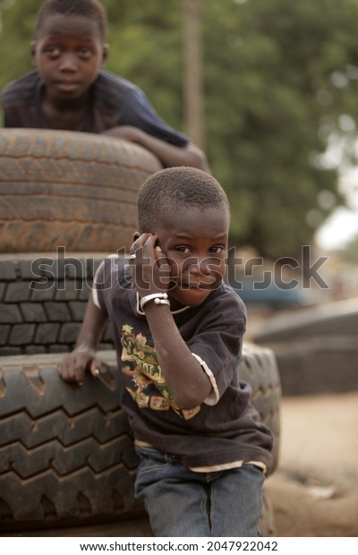 Jarra Soma, the\
Gambia, Africa, June 20, 2021, photography of small african boys in\
dark clothes, posing in front of a pile of used black tires,\
outdoors on a sunny day