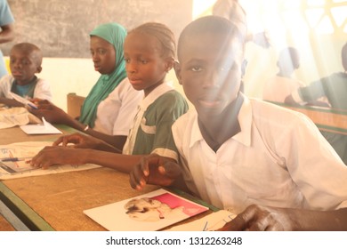 Jarra Soma Region, The Gambia, Africa; March 17, 2017: Horizontal Closeup Of  Elementary School Students In White And Green Uniforms, Sitting By Vintage Desks, On Sunny Day