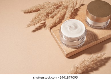 Jars of cosmetic cream with pampas grass on pastel beige background, copy space. Nourishing beauty products, rich anti-age cream.