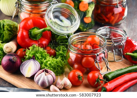Jars with marinated food and raw vegetables on cutting board.