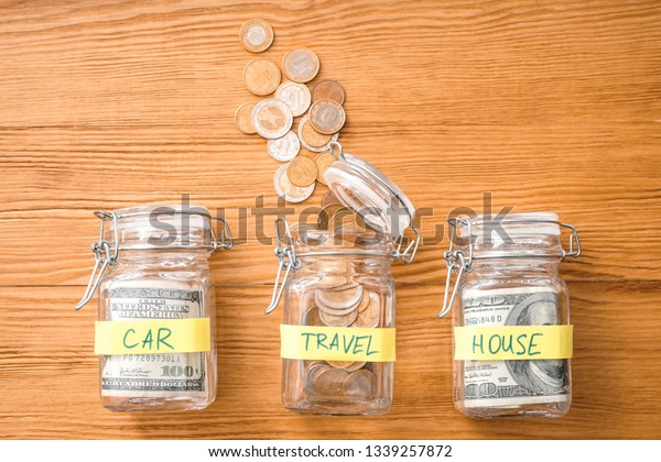 Jars with money for different needs on wooden\
background. Savings\
concept