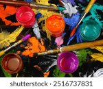 Jars with multi-colored paints, brushes are on a black cloth with spots of different shapes and colors from gouache and acrylic paints, background