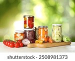 Jars with pickled vegetables on white wooden table outdoors