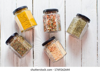 Jars With Various Spices And Herbs, Overhead On White Wooden Background.