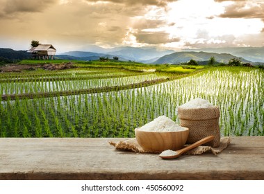 Jasmine Rice In Bowl And Sack On Wooden Table With The Rice Field Background