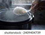 Jasmine rice cooking in electric rice cooker with steam on dark background. Soft Focus,