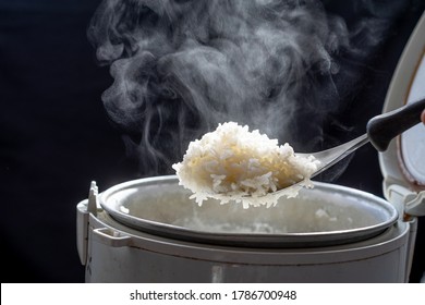 Jasmine rice cooking in electric rice cooker with steam on dark background. Soft Focus,