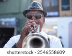 Jazz artist outdoors concert. A mature man with black hat playing a trumpet in the street. Male street trumpet player. Focus on fingers