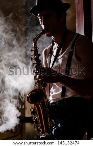Jazz is his life. Handsome young jazzmen playing sax with a smoke on the background