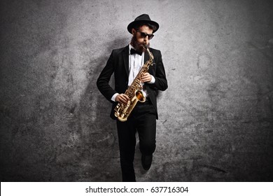Jazz musician playing a saxophone and leaning against a rusty gray wall