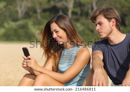 Jealous boyfriend watching his girlfriend texting on the phone on the beach