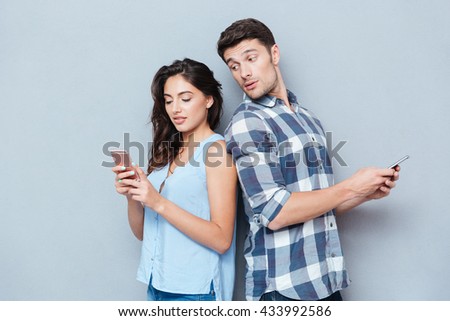 Jealous boyfriend watching his girlfriend texting on the phone isolated on gray background