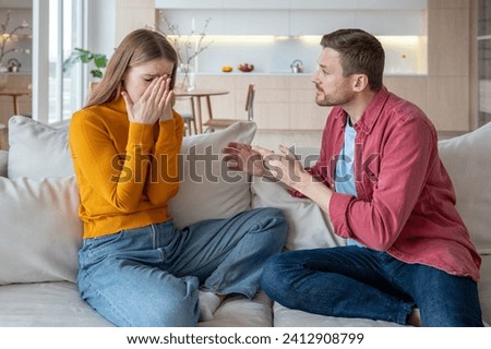 Jealous furious man talk scream at crying woman wife sitting on couch at home. Family quarrel, scandal of two spouses. Tyrant husband threatens woman. Betrayal infidelity mistrust, couple relations.