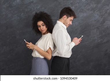 Jealous girlfriend watching her boyfriend texting on phone, social network addiction concept, gray studio background, copy space