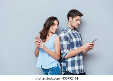 Jealous girlfriend watching his boyfriend texting on the phone isolated on gray background