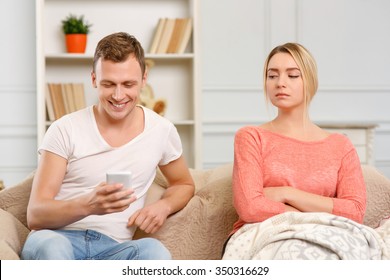 Jealous girlfriend. Young woman looks suspicious while her boyfriend is texting on smartphone.