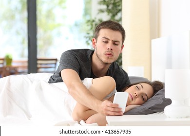 Jealous husband spying the phone of his partner while she is sleeping in a bed at home