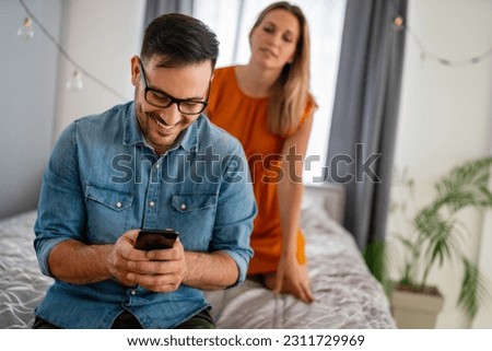 Jealous woman spying boyfriend and watching his mobile phone. Couple cheating jealousy concept