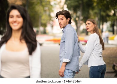 Jealousy. Jealous Girlfriend Calling Boyfriend Distracted By Other Attractive Woman Walking During Date In Park. Selective Focus