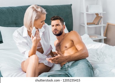 Jealousy Woman With Smartphone Having Quarrel With Her Angry Boyfriend In Bedroom