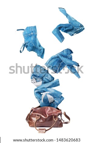 Jeans clothes flying from broun skin luggage bag isolated on a white background