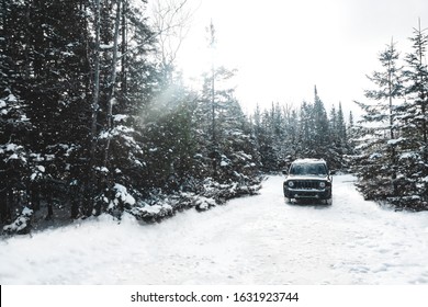 A Jeep / Truck Driving While It's Snowing Through A Forest, Blizzard In A Remote Area, Driving In The Snow. Michigan And Canada. Tall Pine Trees