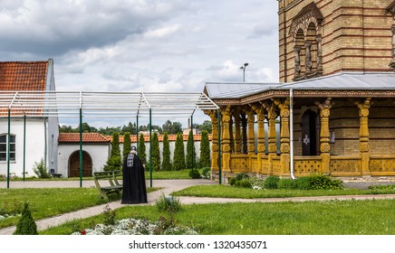 Сourtyard Of Jekabpils Byzantine Style Orthodox Church Of The Holy Spirit In Latvia In Cloudy Summer Day. Priest In Black Long Robe Going Towards Church. 