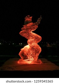 Jelgava / Latvia - February 10th, 2017: Small Carved Ice Sculpture Of A Woman With A Boat In Her Hair  At Night Of International Ice Sculpture Festival In Jelgava - Orange Light