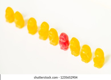 Jelly Baby Confectionary Sweets In A Row. One Is Red The Others Are Yellow. The Background Is White. Individuality Or Discrimination Concept.