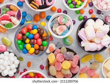Jelly sugar gums candies on blue table with liquorice allsorts and strawberry marshmallow and large variety of sweets and candies. Top view
