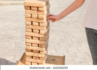 Jenga Puzzle Made Of Wooden Blocks. Outdoor Play, Entertainment. A Young Girl Takes Out A Detail. Tower Of Wood. Pastime In The Company.