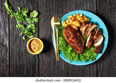 Jerk chicken breasts with grilled ananas cubes and fresh green leaves lettuce on a blue plate on a wooden table, flat lay