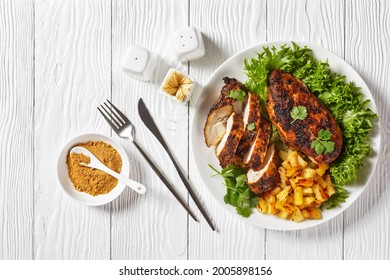 Jerk chicken breasts with grilled ananas cubes and fresh green leaves lettuce on a white plate on a wooden textured table, horizontal view from above, flat lay, free space