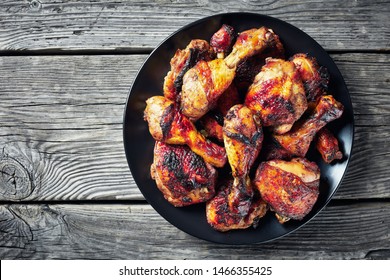 Jerk Chicken on a black plate on a rustic wooden table, horizontal view from above, close-up, flatlay, copy space