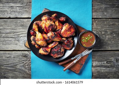 Jerk Chicken on a black plate on a table mat on a rustic wooden table, horizontal view from above, close-up, flatlay, copy space