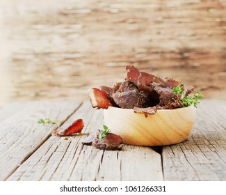 jerked dried meat, cow, deer, wild beast or biltong in wooden bowls on a rustic table, selective focus