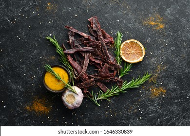 Jerky. Dried meat slices with spices and herbs. Snacks for beer On a black stone background. Top view.
