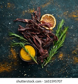 Jerky. Dried meat slices with spices and herbs. Snacks for beer On a black stone background. Top view.
