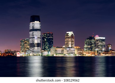 Jersey City Skyline With Skyscrapers At Night Over Hudson River Viewed From New York City Manhattan Downtown.