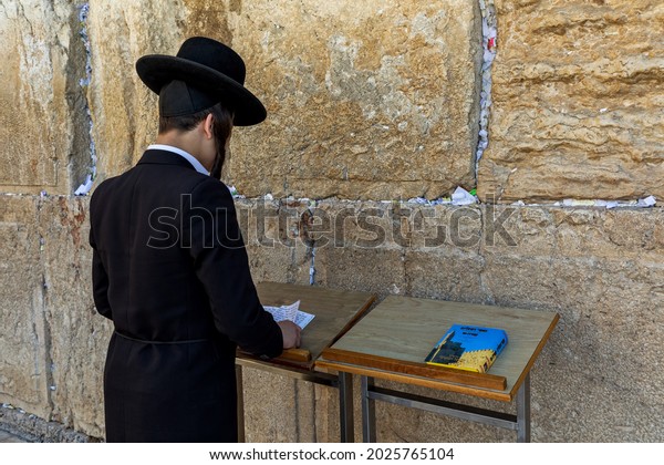 JERUSALEM, ISRAEL - JULY 14, 2019: Jewish\
orthodox man in traditional black wear praying at Wailing Wall (aka\
Kotel) - ancient wall in Old City of Jerusalem, one of the most\
sacred place in\
Judaism.