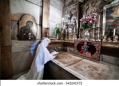 Jerusalem, Israel - July 26, 2014: A nun prays on her knees inside the Edicula, a chapel built on the top of the place recognized as a tomb of Jesus Christ in Holy Sepulchre Church in Jerusalem. 